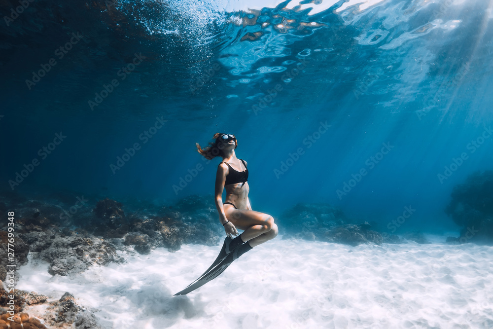 Woman freediver posing over sandy sea with fins. Freediving in Hawaii