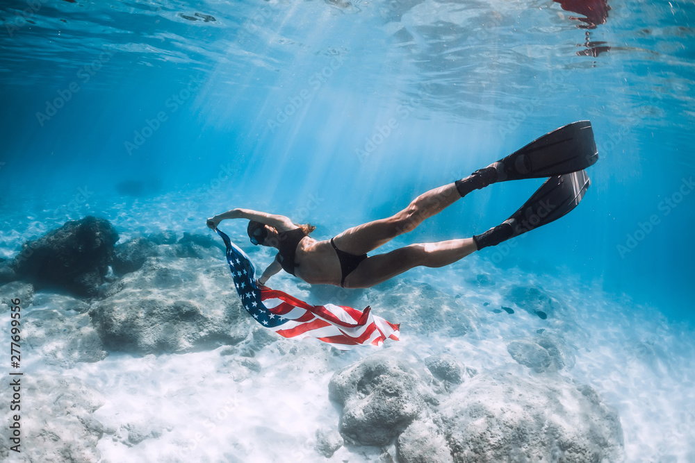 Woman freediver glides over sandy sea bottom with United States flag. Independence day. Woman freediver glides over sandy sea bottom with United States flag. Independence day.