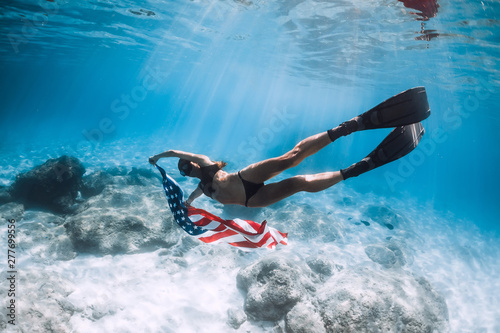 Woman freediver glides over sandy sea bottom with United States flag. Independence day.