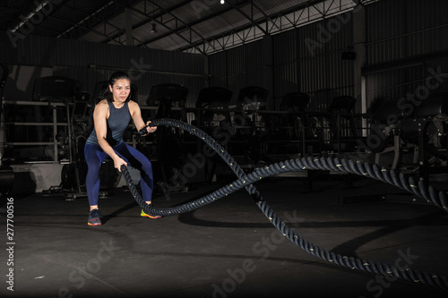 Athletic young woman with battle rope doing exercise in functional training fitness gym.