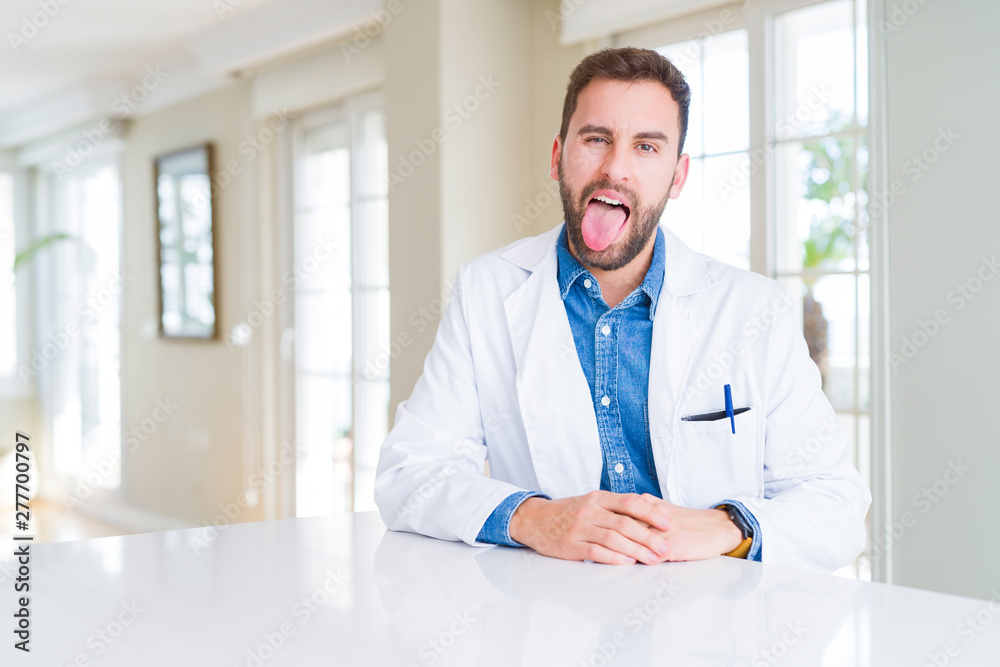 Handsome doctor man wearing medical coat at the clinic sticking tongue out happy with funny expression. Emotion concept. Handsome doctor man wearing medical coat at the clinic sticking tongue out happy with funny expression. Emotion concept.