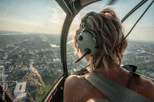 Portrait of beautiful blonde women enjoying helicopter flight. She is amazed by cityscape.