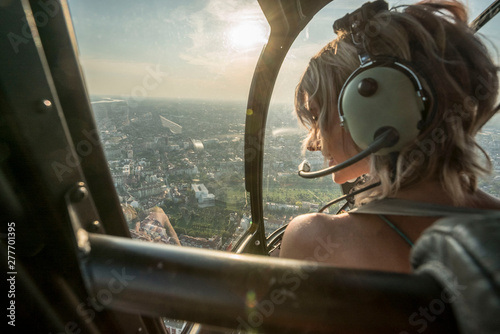 Portrait of beautiful blonde women enjoying helicopter flight. She is amazed by cityscape.