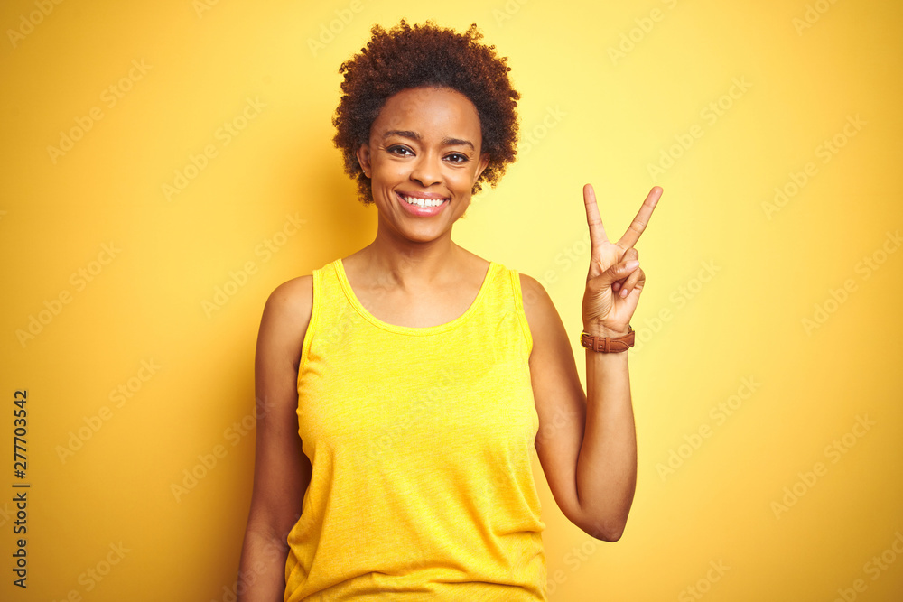 Beauitul african american woman wearing summer t-shirt over isolated yellow background showing and pointing up with fingers number two while smiling confident and happy. Beauitul african american woman wearing summer t-shirt over isolated yellow background showing and pointing up with fingers number two while smiling confident and happy.