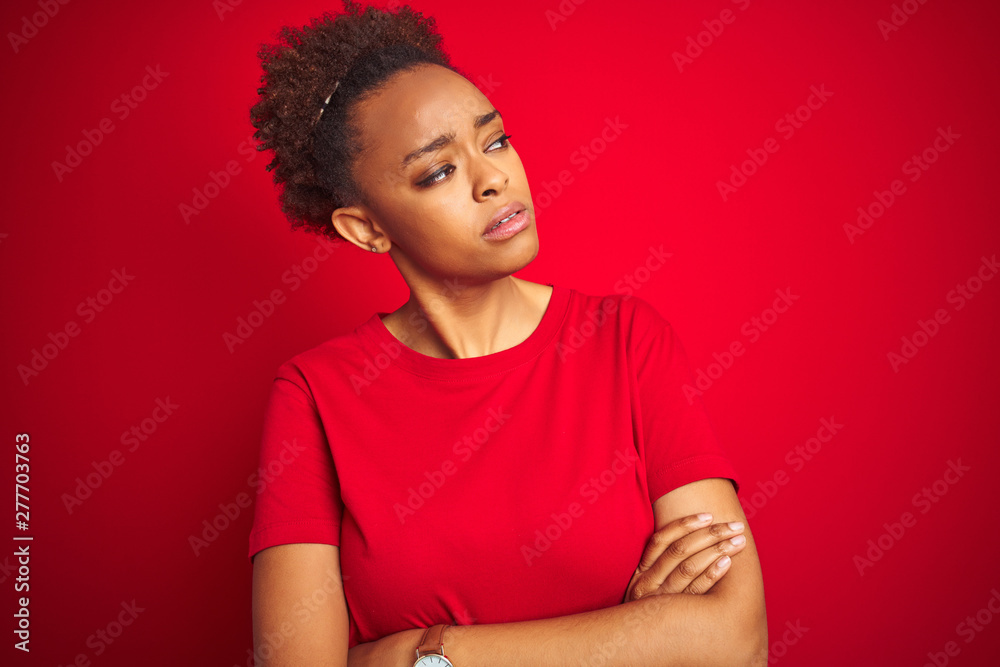 Young beautiful african american woman with afro hair over isolated red background looking to the side with arms crossed convinced and confident Young beautiful african american woman with afro hair over isolated red background looking to the side with arms crossed convinced and confident