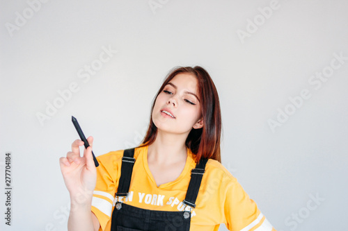 Young smiling girl student worker with dark long hair in yellow t-shirt with graphic pen in hand, isolated on grey background