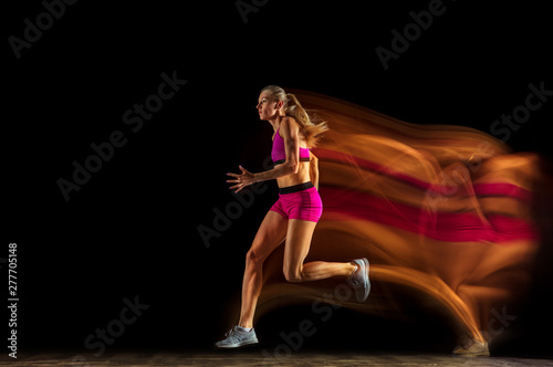 Professional female relay racer training isolated on black studio background in mixed light. Woman in sportsuit practicing in running. Healthy lifestyle, sport, workout, motion, action concept. © master1305