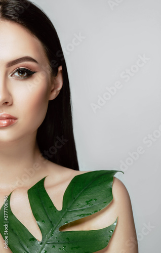 Woman with perfect makeup with arrow on eye and green tropical leaf. Natural organic cosmetic