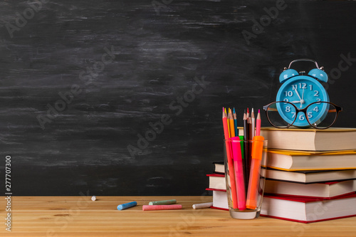 Back to school background with books, alarm clock, eyeglass, color pencil and apple over blackboard.