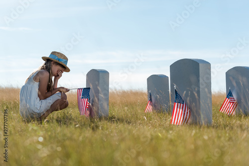 Canvas Print selective focus of child covering face while sitting near headstones with americ