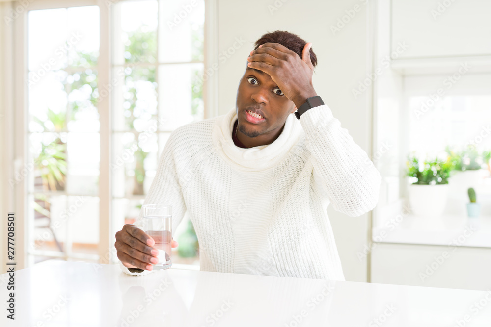 African american man driking a fresh glass of water stressed with hand on head, shocked with shame and surprise face, angry and frustrated. Fear and upset for mistake.