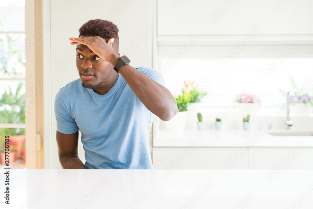 Handsome african american man wearing casual t-shirt at home very happy and smiling looking far away with hand over head. Searching concept.