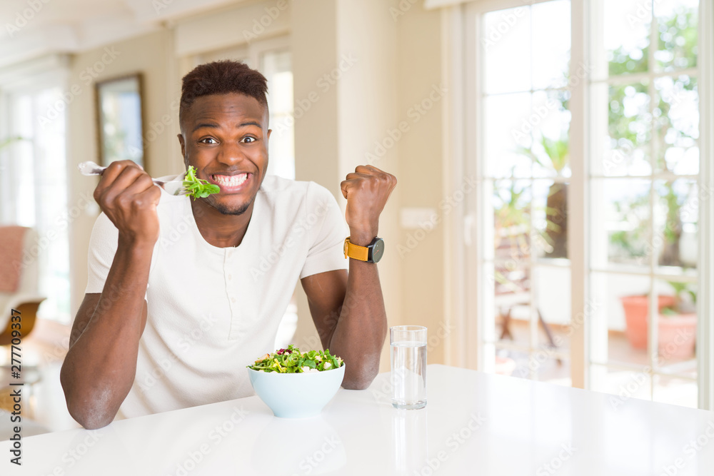 African american man eating fresh healthy salad screaming proud and celebrating victory and success very excited, cheering emotion