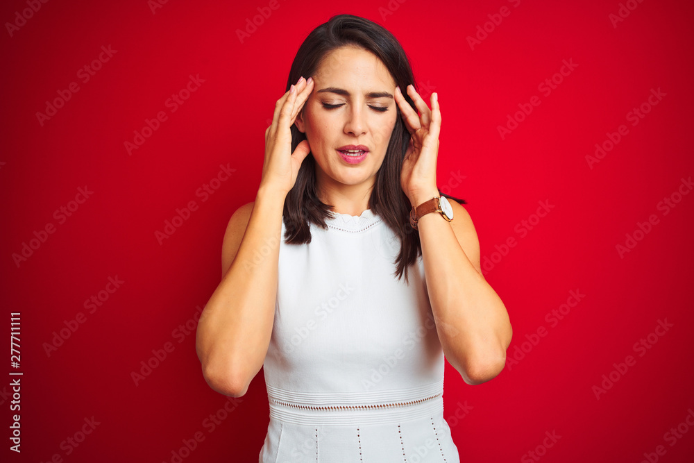 Young beautiful woman wearing white dress standing over red isolated background with hand on head for pain in head because stress. Suffering migraine. Young beautiful woman wearing white dress standing over red isolated background with hand on head for pain in head because stress. Suffering migraine.