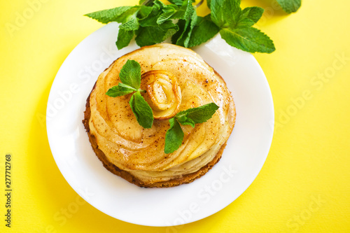 On a white plate lies a cake of apple charlotte close-up. The plate stands on a yellow background, next to it are sprigs of fresh mint.