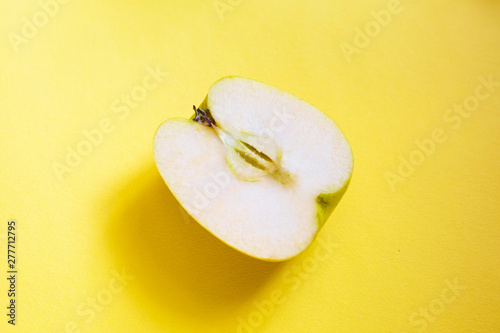 фотографія On a yellow monochromatic background, half a green apple lies diagonally in the center of the center