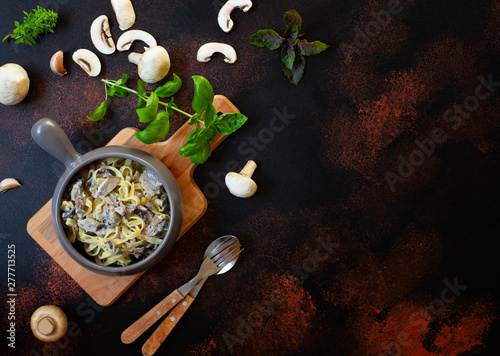 Homemade Italian fettuccine pasta with mushrooms and cream sauce served on a gray pan with basil (Fettuccine al Funghi Porcini). Italian cuisine. Dark rustic background, top view, copy space
