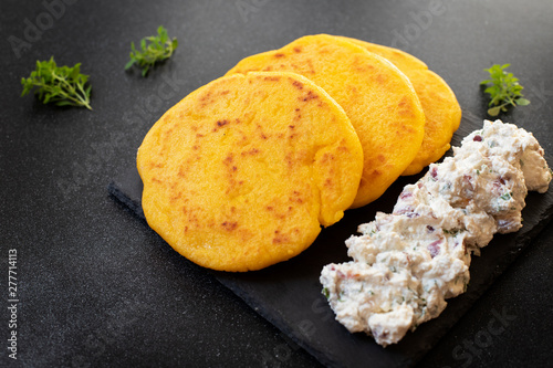 Latin American breakfast Arepas (arepa) of ground maize dough with cheese and herbs served on a black plate. Cuisine of Venezuela and Colombia. Top view, black background, copy space
