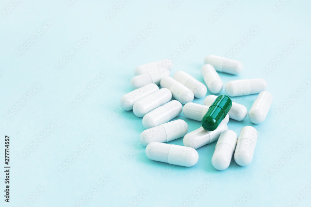  Several white capsules of drugs and pills and one green on a blue background. copy space