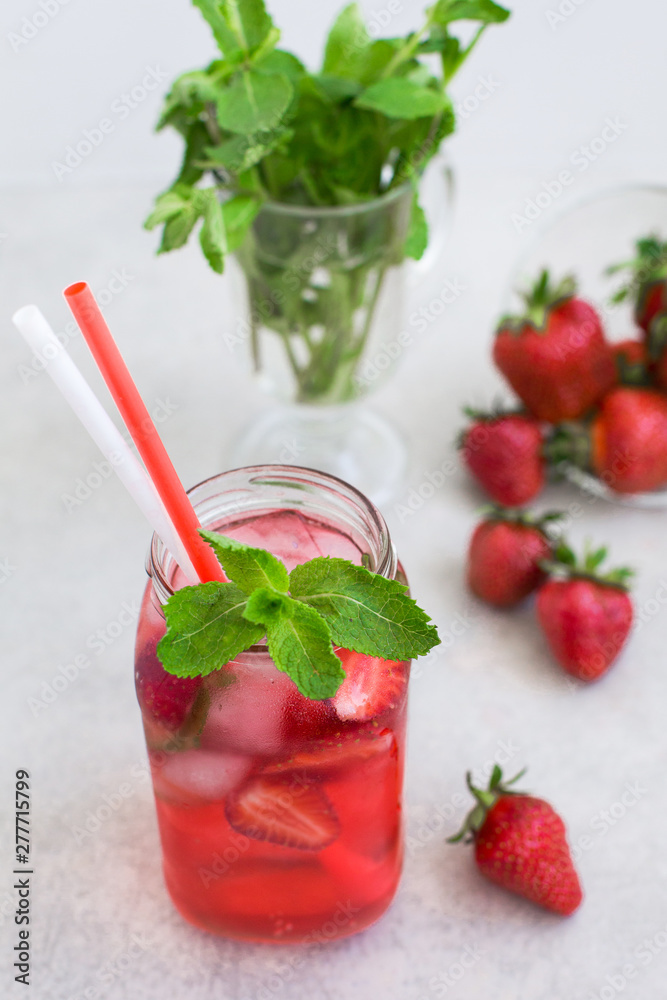 On a light background there is a strawberry cocktail in a glass with ice and mint, a bowl with strawberries On a light background there is a strawberry cocktail in a glass with ice and mint, a bowl with strawberries
