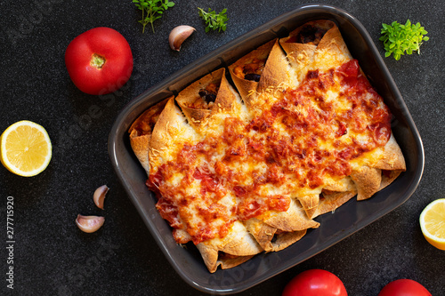 Mexican enchiladas with chicken, vegetables, corn, beans, tomato sauce and cheese. Served in baking tray. Mexican food. Latin American cuisine. Black background, top view, copy space photo