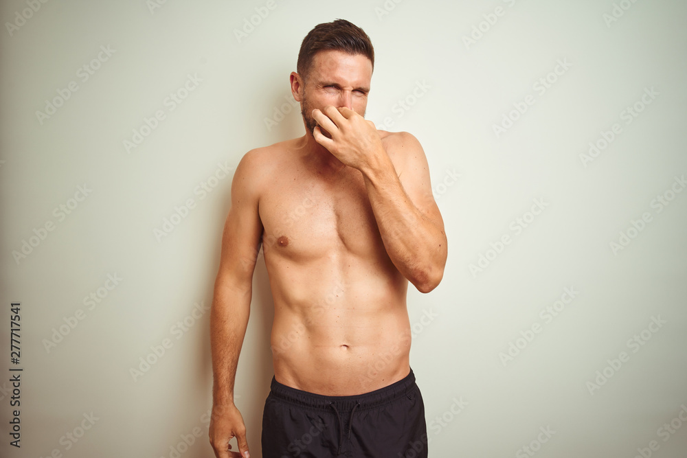 Young handsome shirtless man over isolated background smelling something stinky and disgusting, intolerable smell, holding breath with fingers on nose. Bad smells concept.