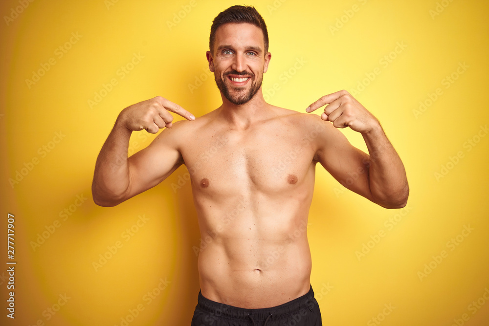 Young handsome shirtless man over isolated yellow background looking confident with smile on face, pointing oneself with fingers proud and happy.