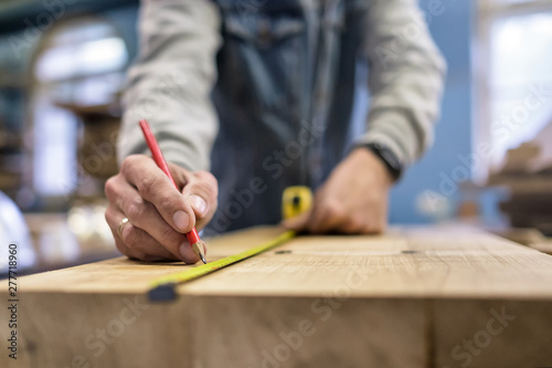 Carpenter measuring and tracing lines with a ruler on a wooden surface. Close up view. Blurred background.