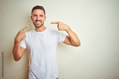 Young handsome man wearing casual white t-shirt over isolated background smiling cheerful showing and pointing with fingers teeth and mouth. Dental health concept. © Krakenimages.com