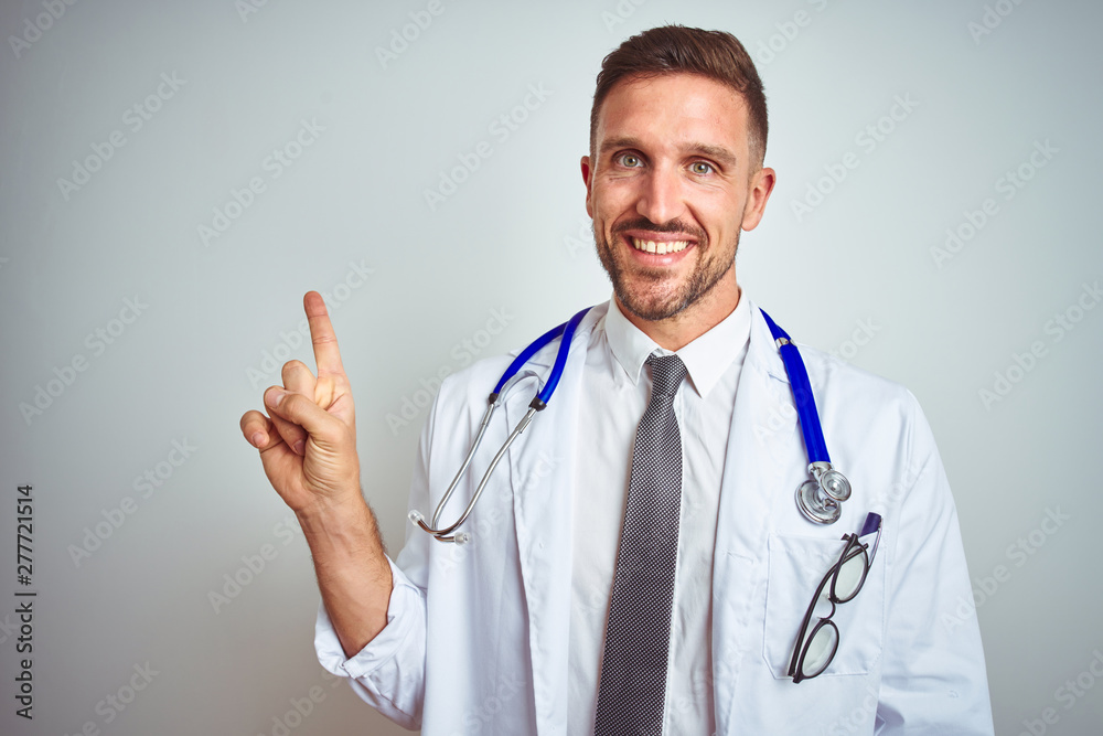 Young handsome doctor man wearing white professional coat over isolated background with a big smile on face, pointing with hand and finger to the side looking at the camera. Young handsome doctor man wearing white professional coat over isolated background with a big smile on face, pointing with hand and finger to the side looking at the camera.