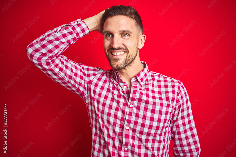 Young handsome man over red isolated background smiling confident touching hair with hand up gesture, posing attractive and fashionable Young handsome man over red isolated background smiling confident touching hair with hand up gesture, posing attractive and fashionable
