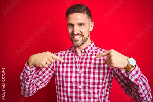 Young handsome man over red isolated background looking confident with smile on face, pointing oneself with fingers proud and happy.