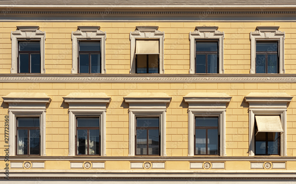 Yellow facade of a beautiful city building. Windows with cornices.
