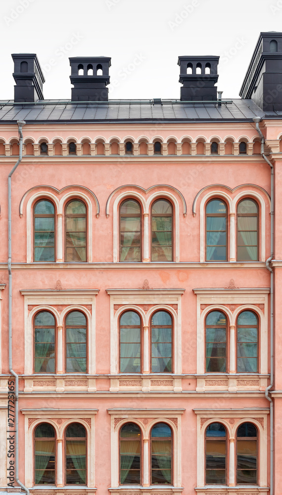 A fragment of the facade of a beautiful pink city building. Windows with a semicircular part