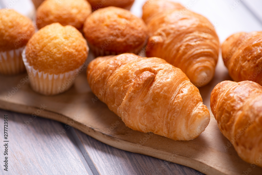 Close-up of cupcakes and croissants prepared for breakfast on wooden board on white wooden table.