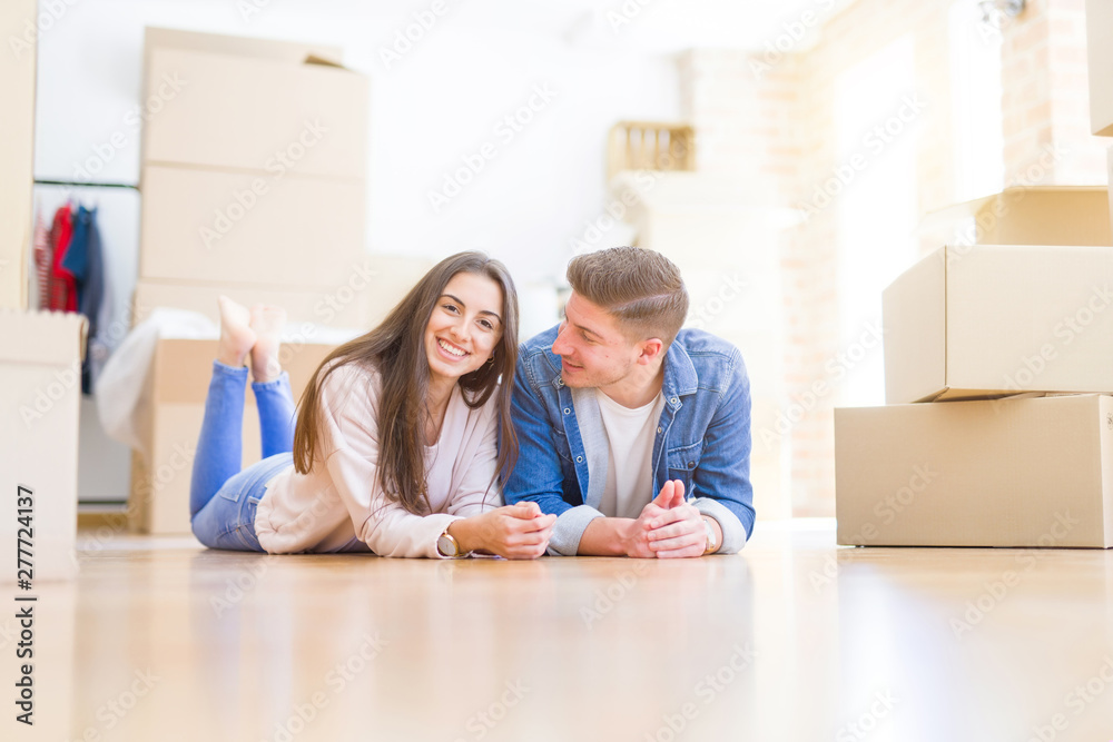 Young beautiful couple relaxing lying on the floor around cardboard boxes at home, smiling happy moving to a new house