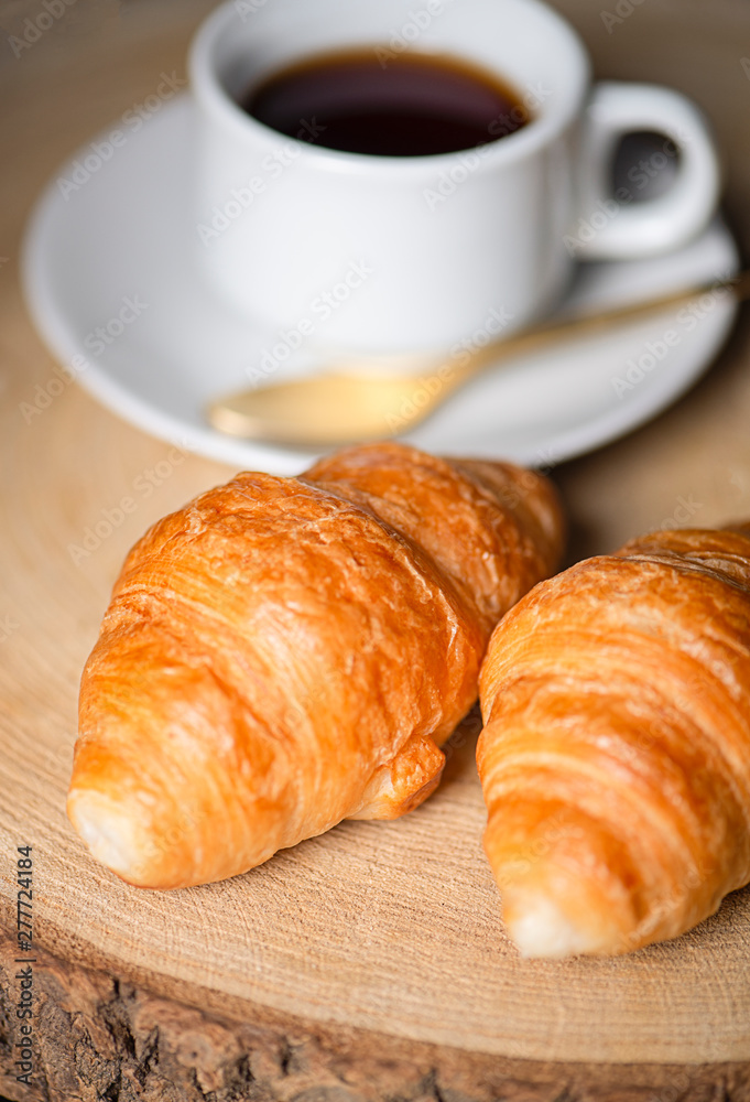 Vertical shoot of two croissants next to cup of coffee on wooden board. Vertical shoot of two croissants next to cup of coffee on wooden board.