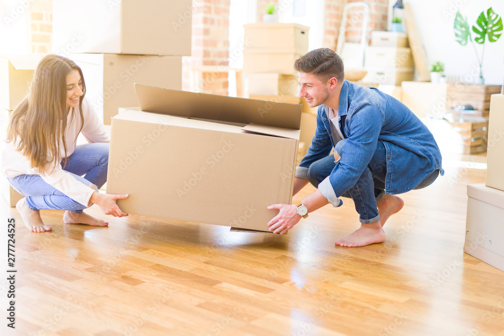 Beautiful young couple smiling in love holding a big cardboard box, happy for moving to a new home Beautiful young couple smiling in love holding a big cardboard box, happy for moving to a new home