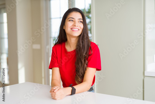 Young beautiful woman at home on white table looking away to side with smile on face, natural expression. Laughing confident. Free Download Young beautiful woman at home on white table looking away to side with smile on face, natural expression. Laughing confident. - GFXLoad