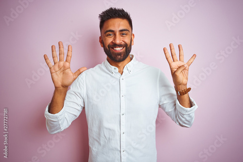 Young indian businessman wearing elegant shirt standing over isolated pink background showing and pointing up with fingers number nine while smiling confident and happy. © Krakenimages.com