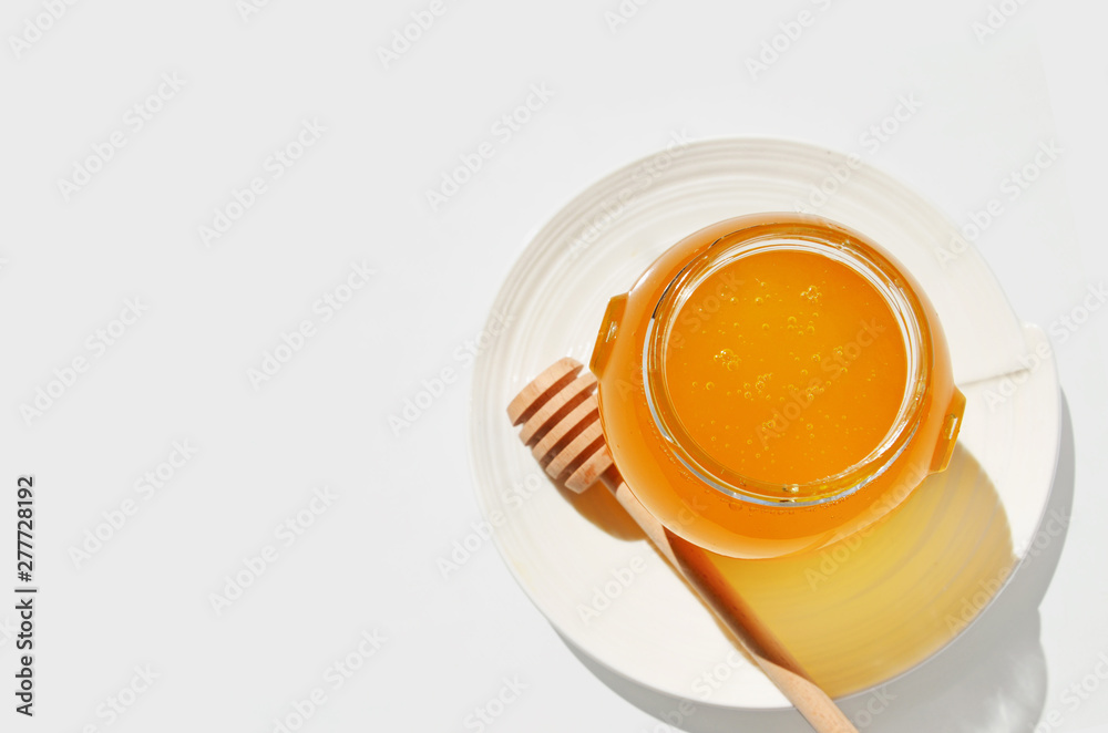 A glass jar of honey and a honey dipper on a saucer. A glass jar of honey and a honey dipper on a saucer.