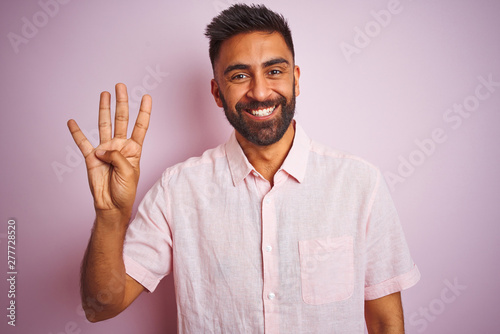 Young indian man wearing casual shirt standing over isolated pink background showing and pointing up with fingers number four while smiling confident and happy.
