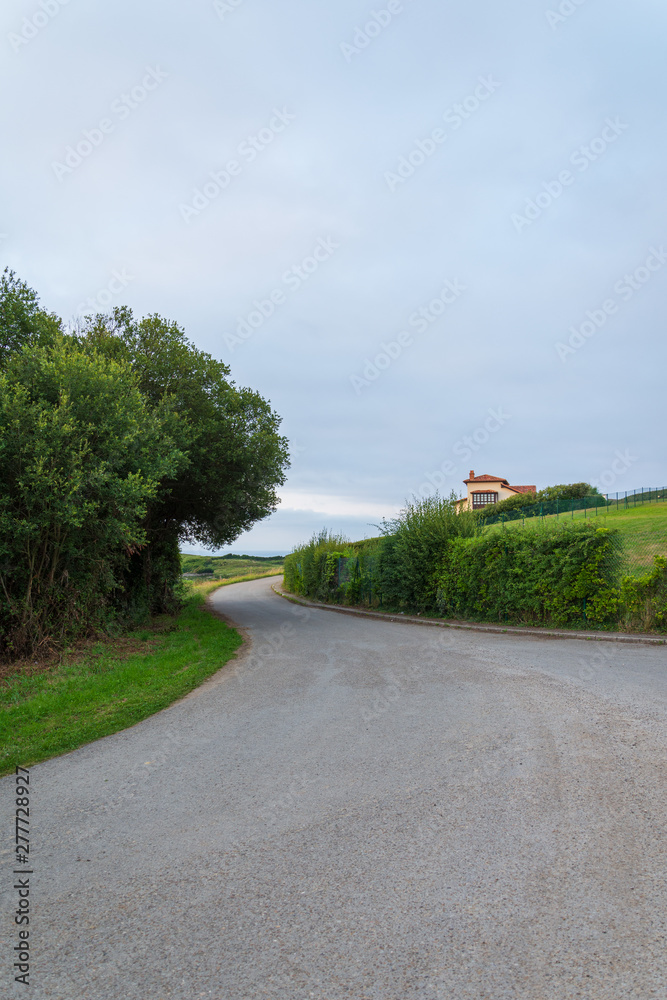 Local road with house, meadows and trees, a cloudy afternoon at sunset in Cantabria, Spain, Europe