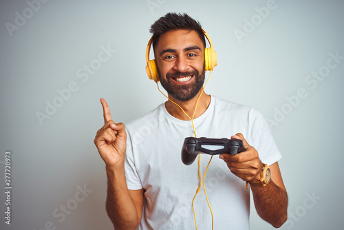 Arab indian gamer man playing video game using headphones over isolated white background very happy pointing with hand and finger to the side photo