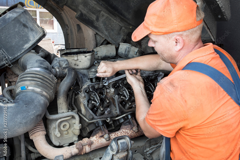 Mechanic repairs a truck. adjustment of valves of the diesel motor