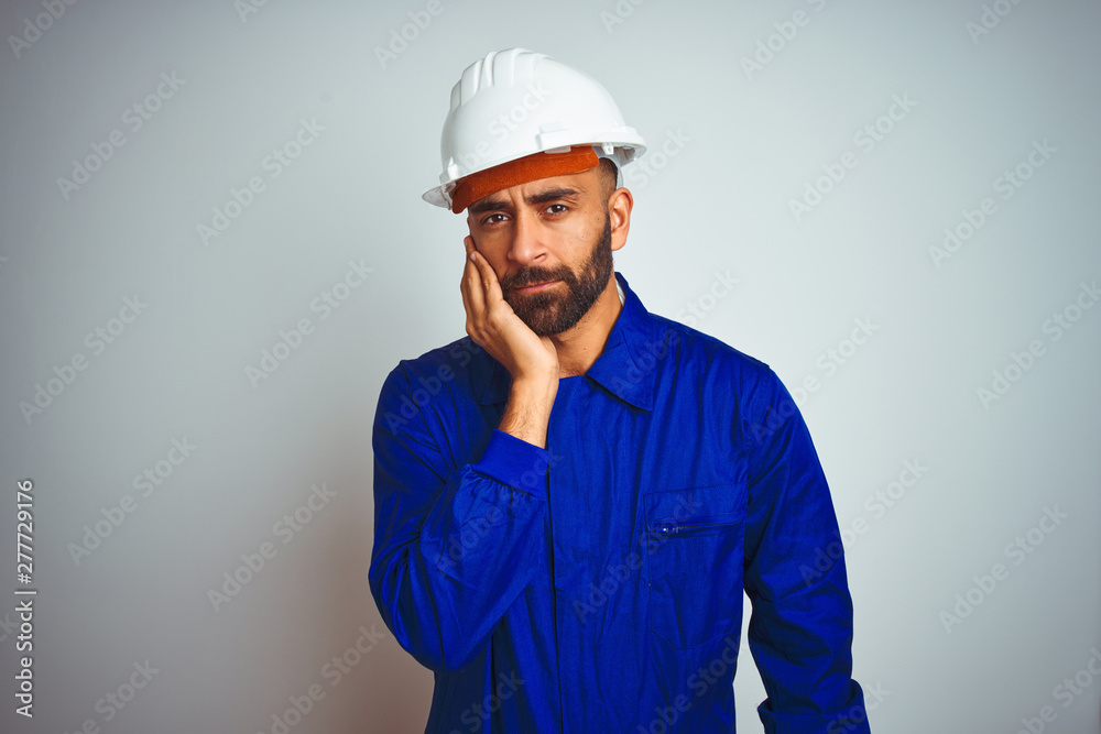 Handsome indian worker man wearing uniform and helmet over isolated white background thinking looking tired and bored with depression problems with crossed arms.