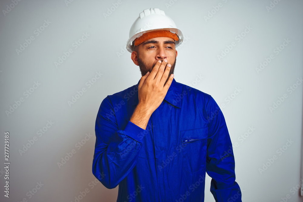 Handsome indian worker man wearing uniform and helmet over isolated white background bored yawning tired covering mouth with hand. Restless and sleepiness.