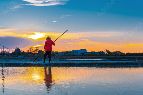 Beautiful sunset scene of salt field. Man farmer working on salt farm in Thailand. Man and the environment in process of salt making in Thailand.