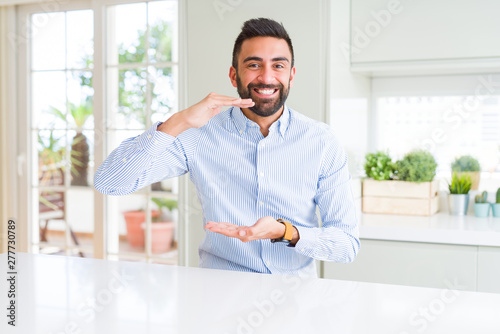 Handsome hispanic business man gesturing with hands showing big and large size sign, measure symbol. Smiling looking at the camera. Measuring concept. © Krakenimages.com