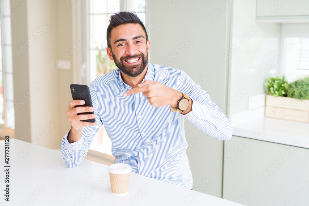 Handsome hispanic business man drinking coffee and using smartphone very happy pointing with hand and finger